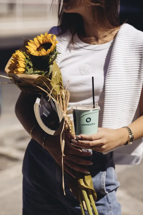 Person holding sunflowers and an iced Kawacom's coffee