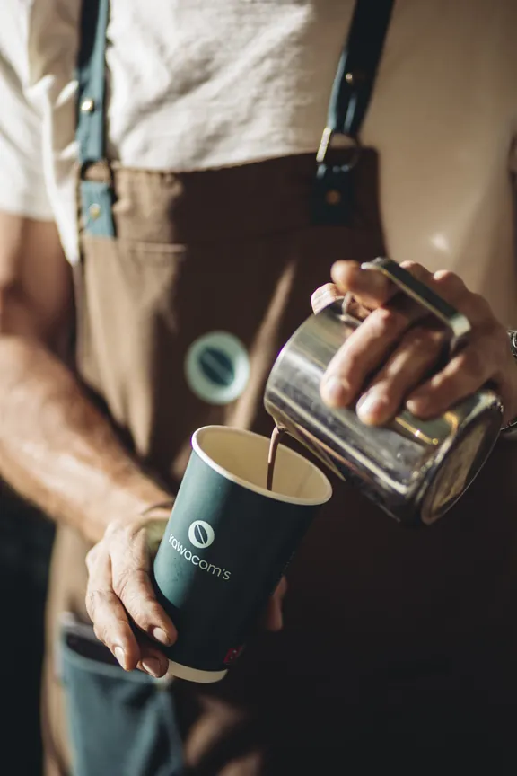 Barista pouring milk into a Kawacom's takeaway cup