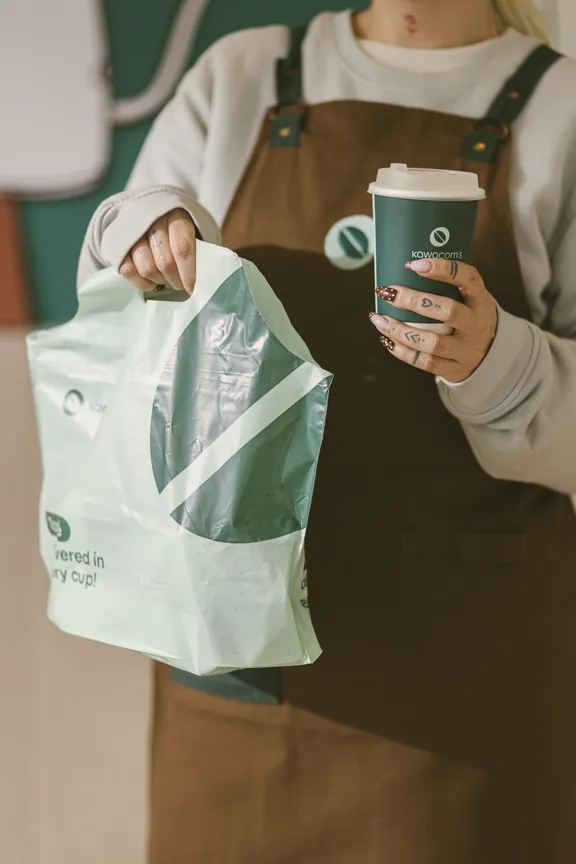 Barista holding a Kawacom's tote bag and a takeaway cup